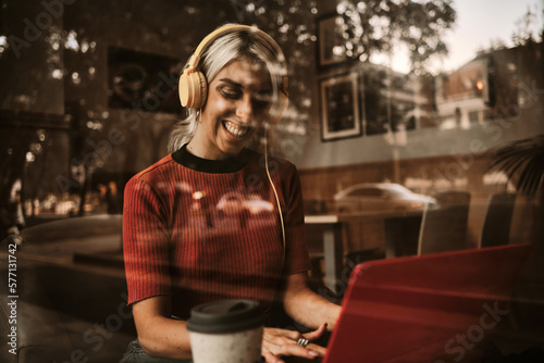 Woman smiling while using headphones and laptop in a coffee shop.