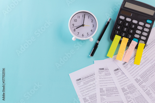 Tax fill concept, clock, pen and sticky notes on calculator  with 1040 U.S. form on blue or green backgound color