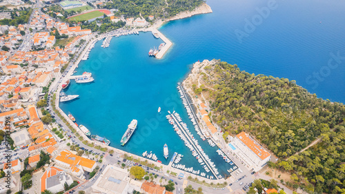 Croatia's harbor is a sight to behold from above. This breathtaking aerial view captures the colorful landscape filled with sailboats, motorboats, and luxurious yachts resting in a clear blue bay. Add