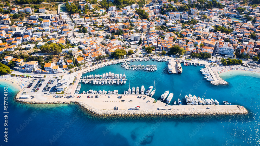 Croatia's harbor is a sight to behold from above. This breathtaking aerial view captures the colorful landscape filled with sailboats, motorboats, and luxurious yachts resting in a clear blue bay. Add