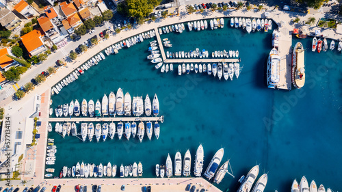 Croatia's harbor is a sight to behold from above. This breathtaking aerial view captures the colorful landscape filled with sailboats, motorboats, and luxurious yachts resting in a clear blue bay. Add
