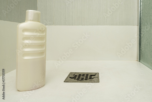 A liter bottle of shampoo inside a shower cabin with a glass partition and white tiles