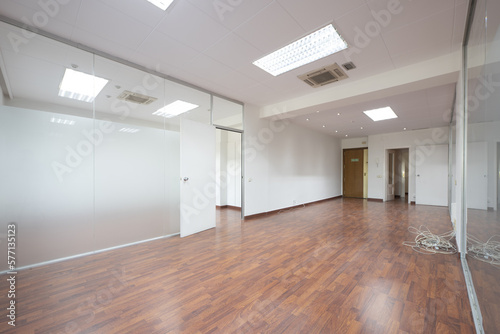 An empty office office with dark wooden floors, technical ceilings and tempered glass partitions
