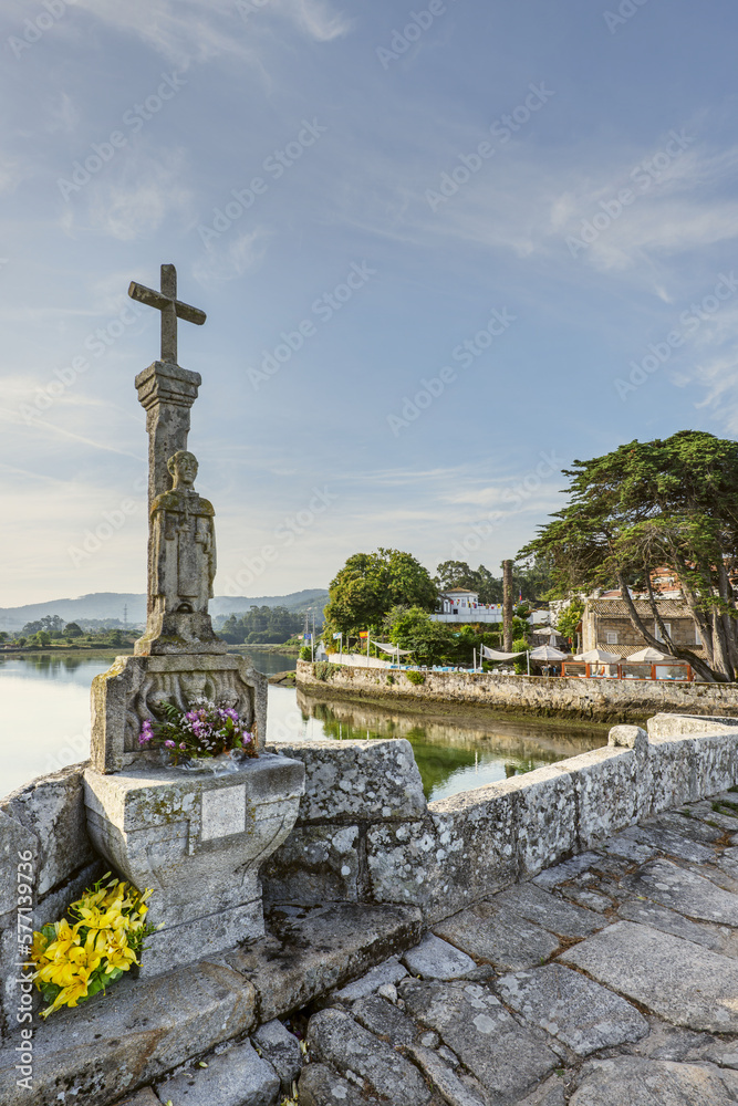 View on the Romanesque bridge of the Miñor river in La Ramallosa that connects Baiona with Nigran in Galicia, Spain a beautiful summer morning with calm water next to a cruise ship with fresh flowers