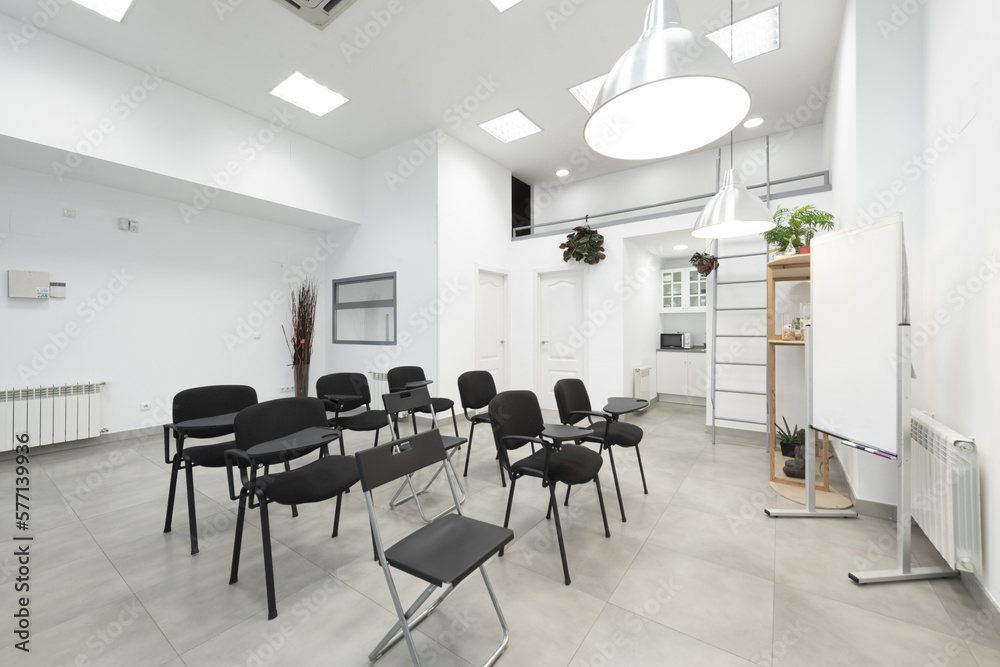Fototapeta premium An empty classroom with a bunch of black chairs with armrests with a swing table, a whiteboard for deleble ink markers