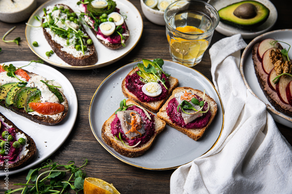 Mix of smorrebrods (open sandwiches) with different toppings: avocado-salmon-cream cheese, herring-beetroot paste, green peas - cottage cheese, quail eggs -beetroot - cream cheese; and mustard sauce 