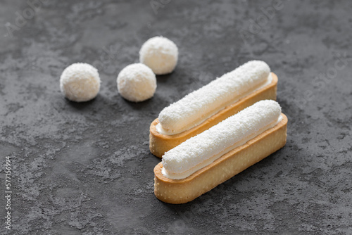 Foto Oval tartlets in the form of eclair Raffaello with coconut custard and cream jelly, sprinkled with coconut chips on top