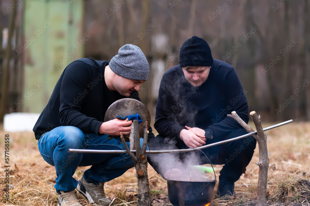 Two guys check the readiness of food on the fire