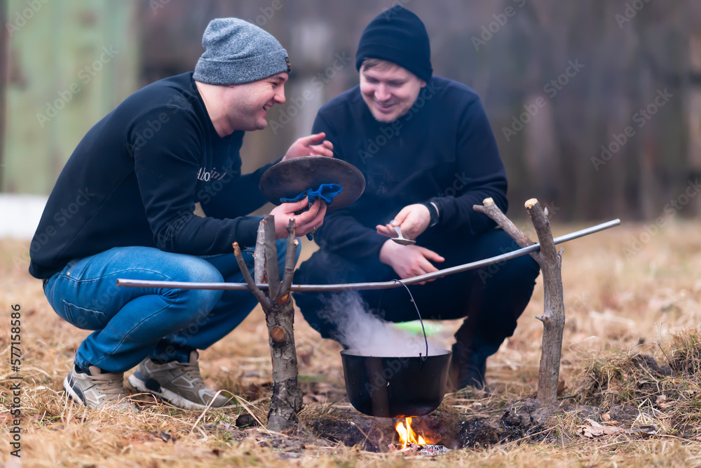 The guys laugh and cook food on a fire
