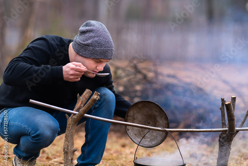Obraz na płótnie A young guy tastes the broth being cooked over a campfire w salonie