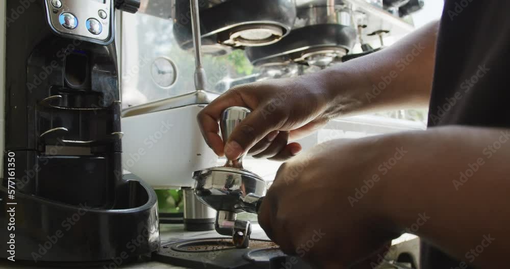 Close up of african american male barista making coffee using coffe machine at cafe