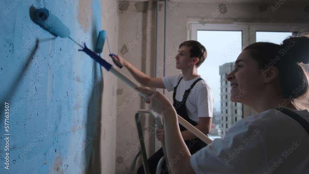 Couple in new home during repair works painting wall together. Happy