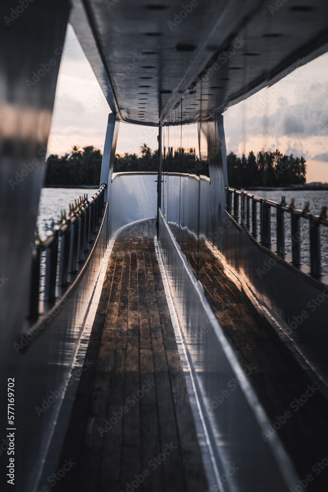 A vertically shot from a boat's deck is a unique capture of a sunset mirrored by the wall of the boat, the serene seascape in the background in shallow depth of field is beautiful