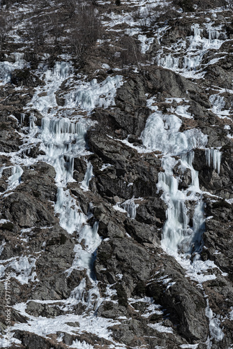 Several frozen water streams forming ice flows and icicles on a dry rocky mountainside in winter in Chamonix, France