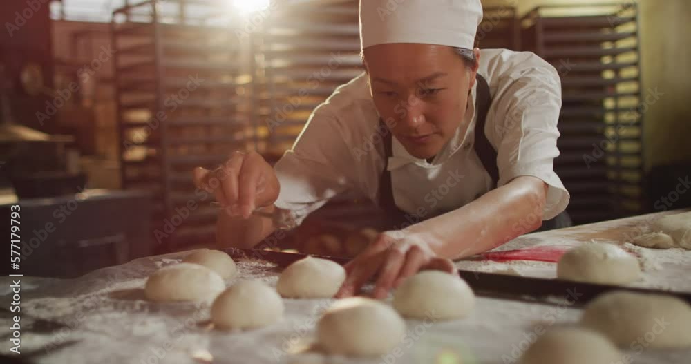 Animation of focused asian female baker arranging rolls on tray