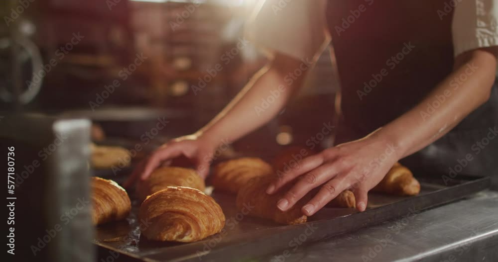 Animation of hands of asian female baker arranging croissants on tray