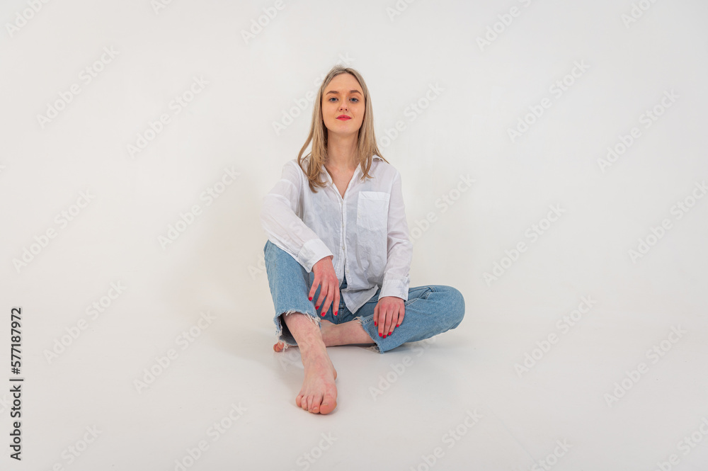 Portrait of a smiling young pretty European woman relaxing while sitting on the floor in jeans and a white shirt, isolated on white background. Place for writing Portrait of a smiling young pretty European woman relaxing while sitting on the floor in jeans and a white shirt, isolated on white background. Place for writing