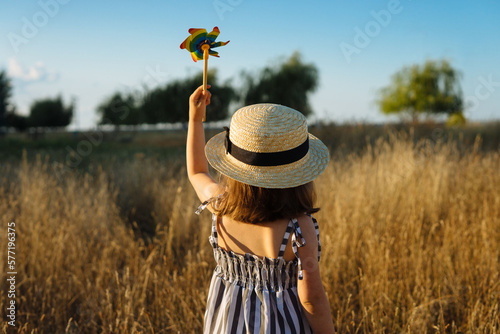 Little girl holding up a pinwheel toy against clear sky in the meadow