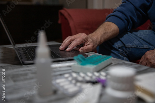 Close-up of a senior's hand using a laptop with medication beside it