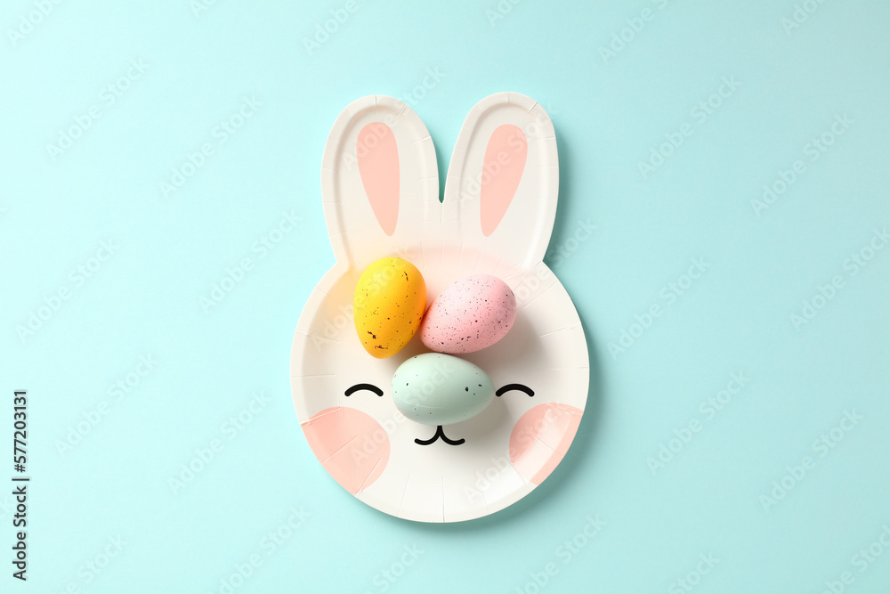 Bunny shaped plate with colorful Easter eggs on pastel blue background. Flat lay, top view. Bunny shaped plate with colorful Easter eggs on pastel blue background. Flat lay, top view.