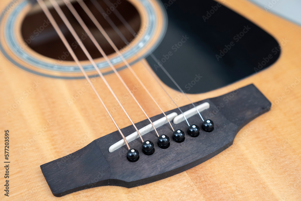 Obraz premium detail of the bridge of a light wood acoustic guitar with its pegs and pins, selective focus, horizontal