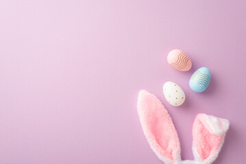 Easter concept. Top view photo of fluffy bunny ears and colorful easter eggs on isolated lilac background with copyspace