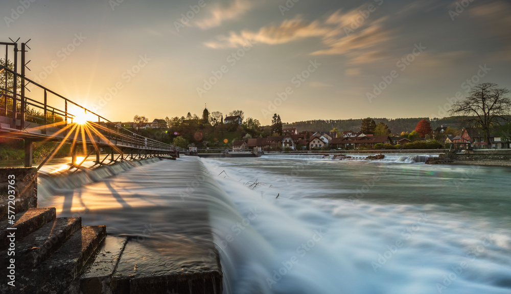 Naklejka premium Schäumendes Wasser beim Streichwehr/Flusstufe in der Reuss bei Unterwindisch. Die Abendsonne scheint durch die Wehrbrücke.