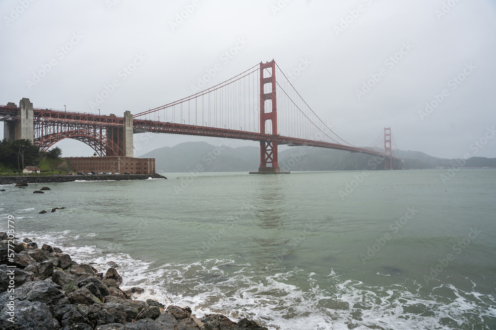 Dramatic image of the Golden Gate Bridge during a rainstorm with a rocky beach in the foreground. Dramatic image of the Golden Gate Bridge during a rainstorm with a rocky beach in the foreground.