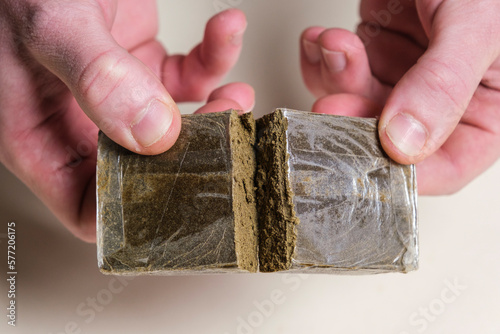 A drug dealer checks the quality of a hashish stick ready for sale on a white background. Medical marijuana extraction dry hashish cannabis pollen.