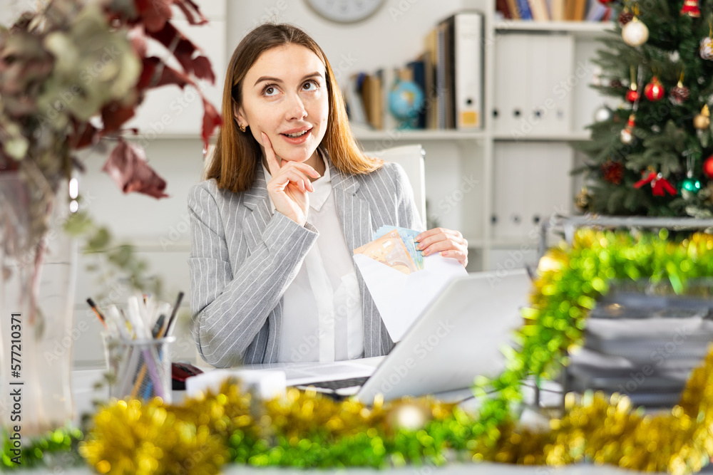 Young woman accountant with wage packet full of cash in Christmas decorated office.