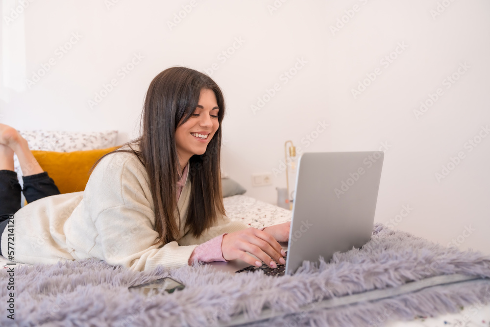 Young woman working with laptop in bed, telecommuting, teleworking, writing an email Young woman working with laptop in bed, telecommuting, teleworking, writing an email