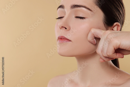 Young woman massaging her face on beige background. Space for text
