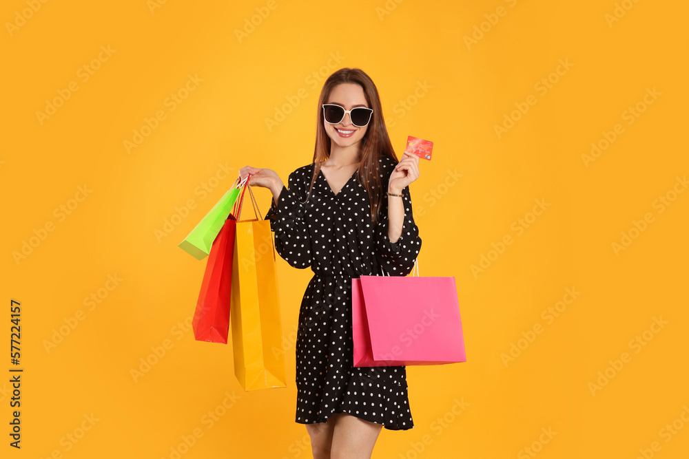 Happy young woman with shopping bags and credit card on yellow background. Big sale - obrazy, fototapety, plakaty 