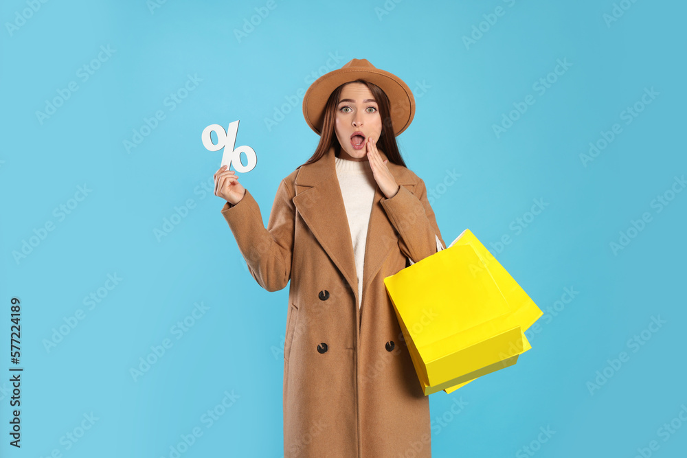 Surprised young woman with shopping bags and percent symbol on light blue background. Big sale Surprised young woman with shopping bags and percent symbol on light blue background. Big sale