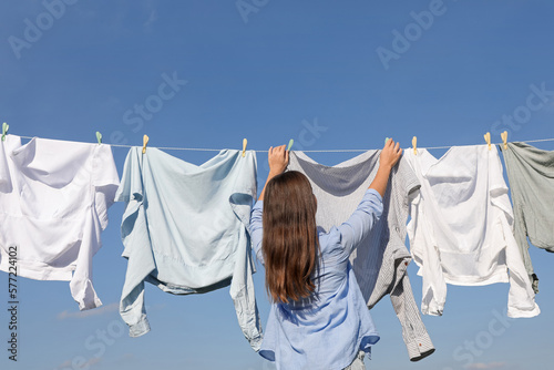 Woman hanging clothes with clothespins on washing line for drying against blue sky, back view