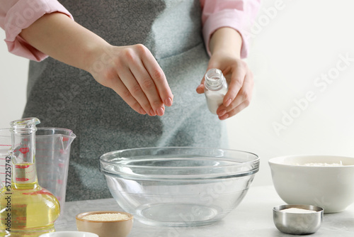 Woman adding pinch of salt into bowl at grey marble table indoors, closeup. Cooking traditional grissini
