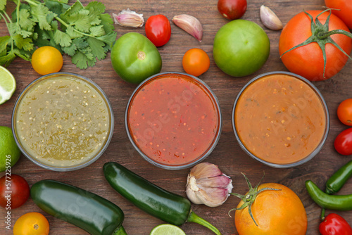 Flat lay composition of tasty salsa sauces and different ingredients on wooden table
