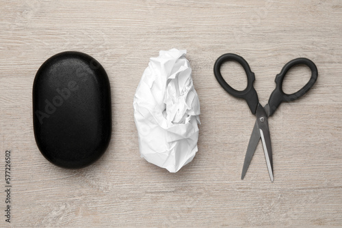 Rock, crumpled paper and scissors on wooden background, flat lay