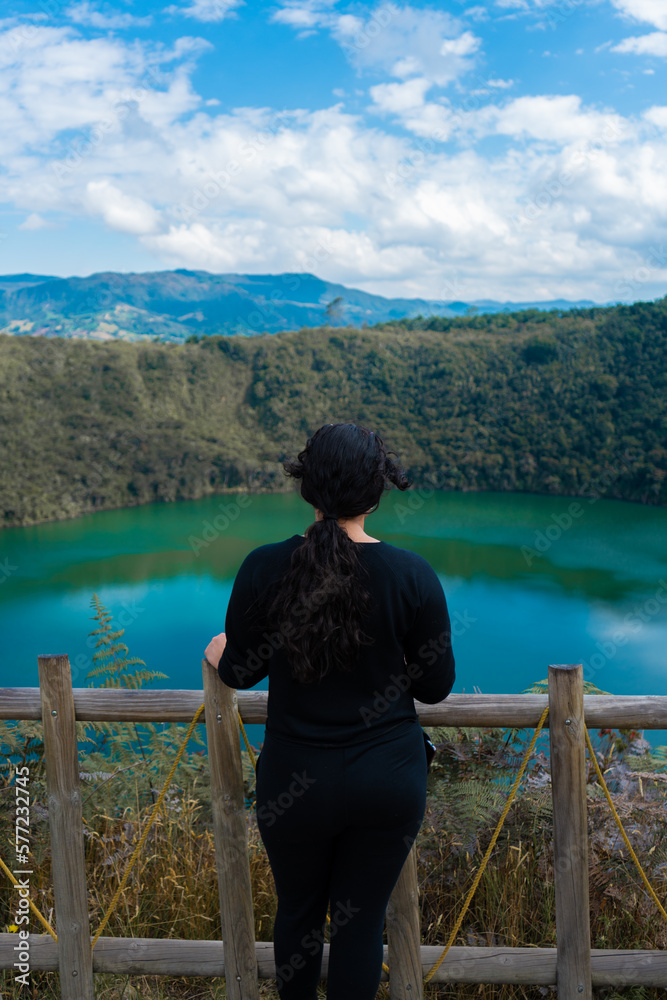 Fototapeta premium Mujer latina pelo negro observando una laguna color esmeralda en un dia soleado