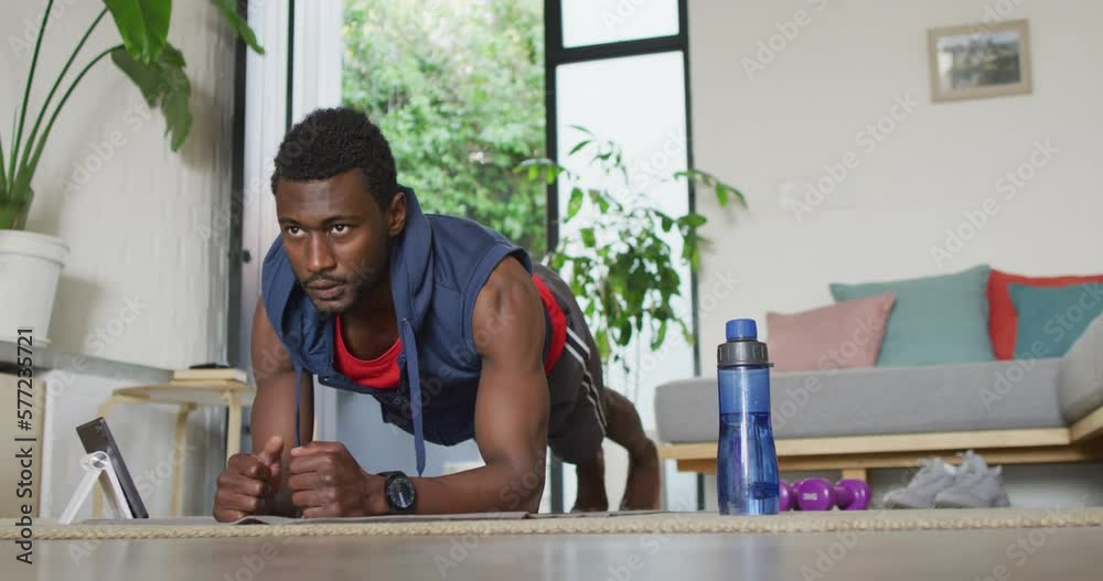 Happy african american man exercising in living room, using tablet Happy african american man exercising in living room, using tablet