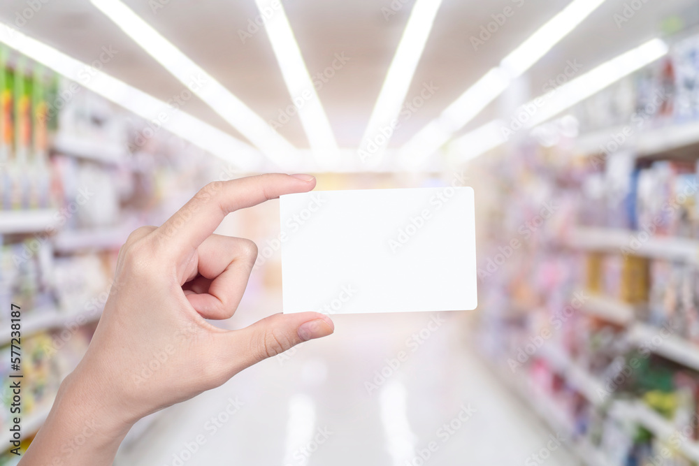 woman hand holding blank white credit card with blurred abstract background of multicolored cotton clothing on the shelves of fashion shop woman hand holding blank white credit card with blurred abstract background of multicolored cotton clothing on the shelves of fashion shop