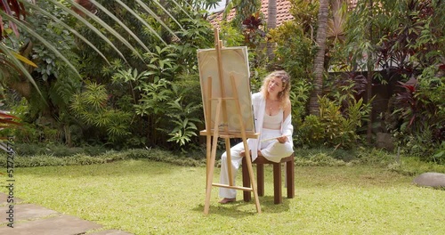 Creative young female artist painting a picture with acrylic paints outdoors. Creativity, hobby and art concept 