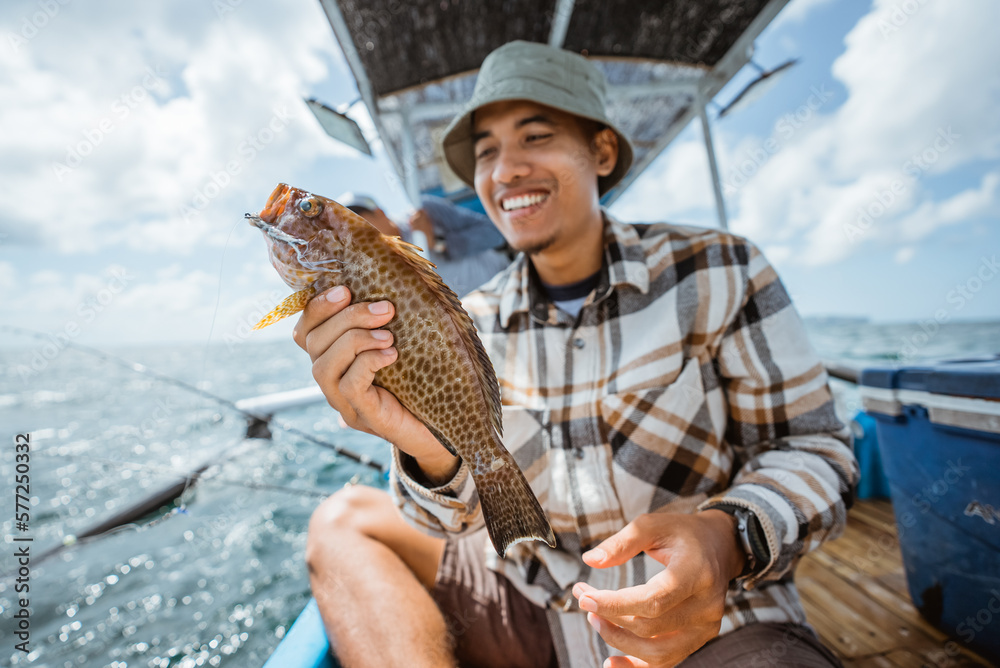 Fototapeta premium strike grouper held by an Asian angler on a small fishing boat