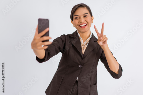 asian woman standing with peace hand gesture while taking selfie photo on isolated background photo