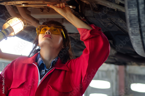 Asian woman auto mechanic work in vehicle repair shop, check and repair under body and suspension system, international Women's day photo