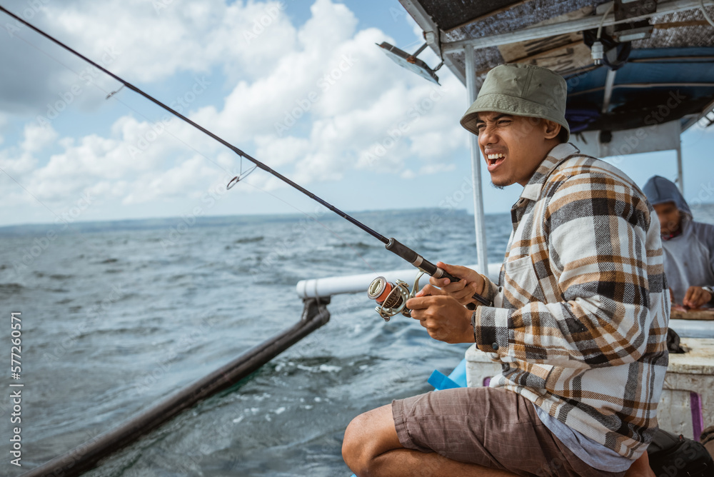 excited angler reels in fishing line while casting on a small fishing boat at sea