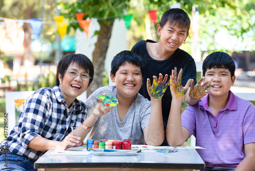 teen students and a female art teacher having fun painting hands while working on a school art project  adult teacher help teenager boys in outdoor art class