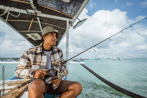 Asian anglers sit with their fishing rods as they set out to fish in a small boat