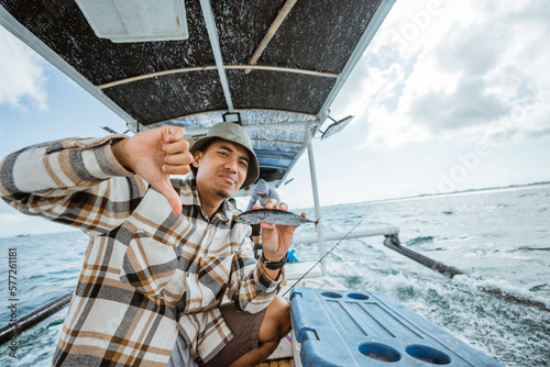 angler is upset by losser's hand gesture while holding a small fish while sea fishing