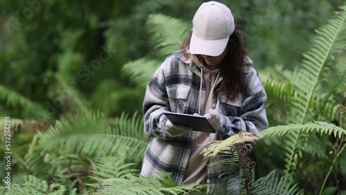 Woman botanist is researching plant species and working on digital tablet in tropical rainforest. Environment and ecosystem concept. Biology activist.